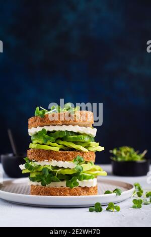 Avocado, Gurken- und Fetakäse-Sandwich mit Micro-Greens und Mehrkornbrot auf einem einfachen Holzständer für ein gesundes Frühstück. Selecti Stockfoto