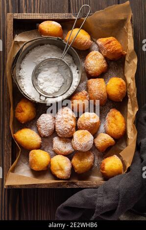 Kleine Donuts. Hausgemachte Hüttenkäse-Kekse in Fett gebraten und mit Puderzucker bestreut in einem alten Holzkästchen Tablett gegen einen alten dunklen Rücken Stockfoto