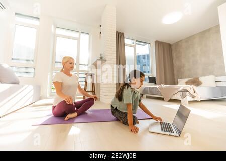 Junge Erwachsene Mutter mit ihrer Tochter beobachten Online-Training zusammen zu Hause, Blick auf einen Laptop Stockfoto