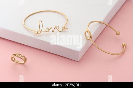 Wort Liebe und Knoten Form Goldene Armbänder und Ring an Rosa und weißes Papier Stockfoto