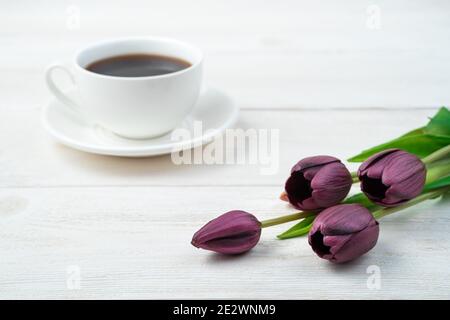 Lila Tulpen und eine weiße Kaffeetasse im Hintergrund auf einem hellen Holzhintergrund. Stockfoto