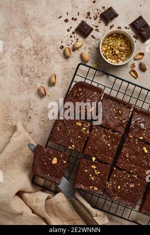 Schokoladenquadrate mit Pistazien und Erdbeeren auf einem Metallständer auf einem hellen Steingrund, Draufsicht, horizontale Komposition. Stockfoto