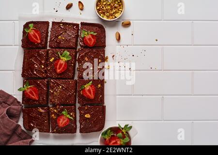 Schokoladenquadrate mit Pistazien und Erdbeeren auf weißem Papier auf hellem Hintergrund, Draufsicht, horizontale Komposition. Stockfoto