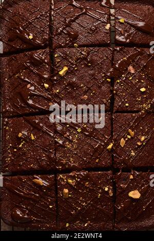 Schokoladenquadrate mit Pistazien und Erdbeeren auf einem Metallständer auf einem hellen Steingrund, Draufsicht, horizontale Komposition. Stockfoto