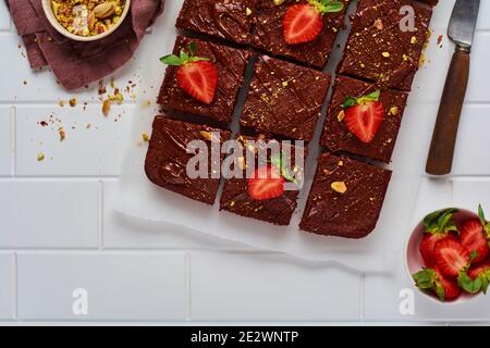 Schokoladenquadrate mit Pistazien und Erdbeeren auf weißem Papier auf hellem Hintergrund, Draufsicht, horizontale Komposition. Stockfoto