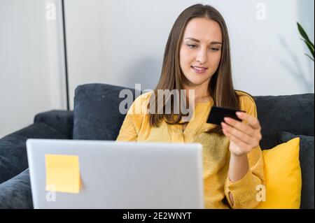 Eine Frau mit Kreditkarte und Laptop kauft online, prüft Transaktionen, erhält Zahlungen auf der Karte, prüft Daten auf einer Karte Stockfoto