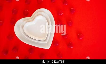 Herz Form weiße Platte auf rotem Hintergrund mit kleinen Süßigkeiten Stockfoto