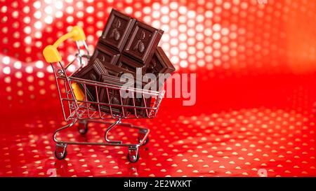 Schokolade im Einkaufswagen auf rotem Hintergrund. Angebot vom 14. februar. Kreatives Minimalkonzept Stockfoto