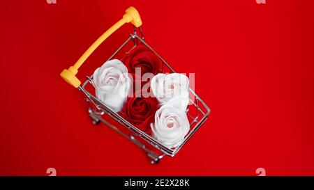Rote und weiße Rosen Blume auf Warenkorb auf rotem Hintergrund. Shopping Urlaub für Valentinstag Liebe Konzept Stockfoto