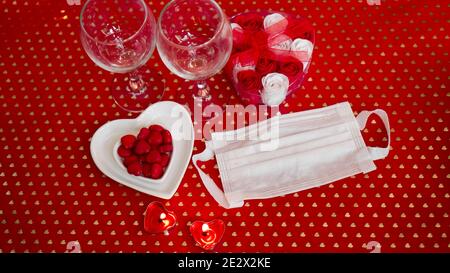 Valentinstag Konzepttisch. Romantisches Abendessen mit medizinischer Maske. Coronavirus 2021. Gesichtsschutzmaske und rote Tischeinstellung Stockfoto