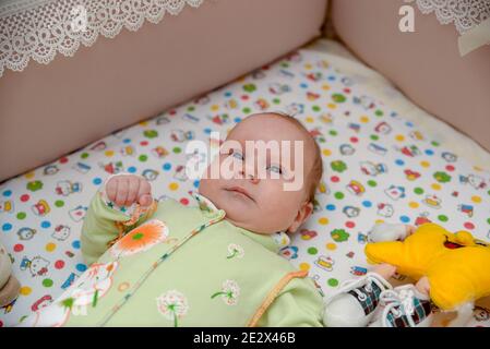 Ein kleines Kind liegt in einem Kinderbett mit Spielzeug Stockfoto