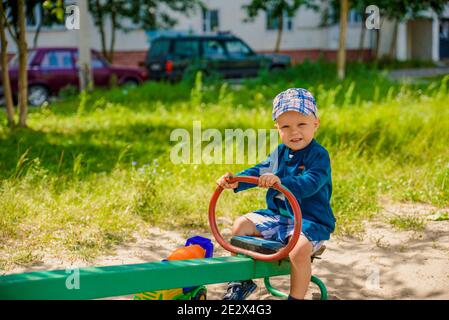 Ein Junge in Shorts und einer Mütze reitet auf einem Schaukel im Sommer Stockfoto