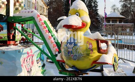 Das leere Karussell ist mit Schnee bedeckt. Nahaufnahme von schneebedeckten bunten Enten Karussell auf Spaß Messe Karneval während des Winters tagsüber Stockfoto