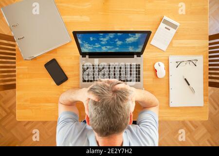 Gestresster Mann sitzt an einem Tisch mit Laptop während der Arbeit Von zu Hause aus - Ansicht von oben - das Foto und das Sreen wurde von mir genommen Stockfoto