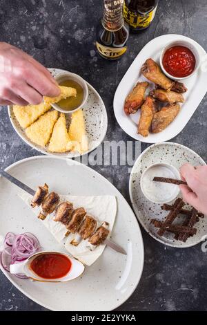 Auf dem Tisch stehen saftige Shish-Kebabs und gegrillte Hähnchenschenkel mit würziger Tomatensauce, Croutons und Käse Stockfoto