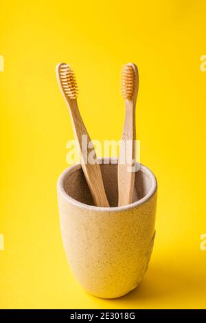 Becher mit zwei Bamboo Bio-Zahnbürsten für die Zahnhygiene auf Trendy gelben Hintergrund - umweltfreundliche Null Abfall Kunststoff frei Konzept Biologisch abbaubar m Stockfoto