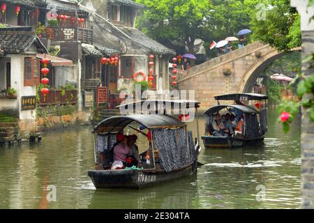 Touristenboote in Xitang führen Touristen entlang des alten Kanals. Schöne Szene auch im Regen, aufgehellt durch all die roten Laternen. Stockfoto