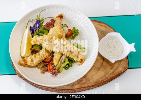 Gebutterter Fisch und grüner Salat mit Sauce und Zitrone, verziert mit Schmetterlingsblüten. Serviert auf einer weißen Keramikplatte. Stockfoto