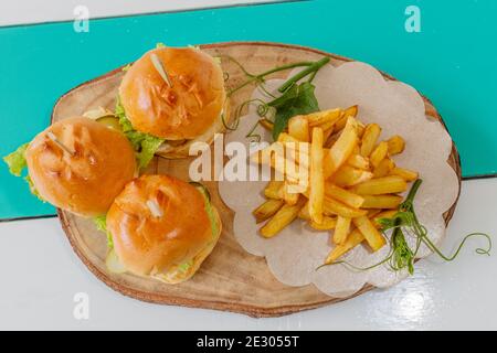 Drei Fischschuppen (Mini-Burger) mit Salat, Tomaten und Gurken, serviert mit pommes frites auf einem Holztablett. Draufsicht. Stockfoto