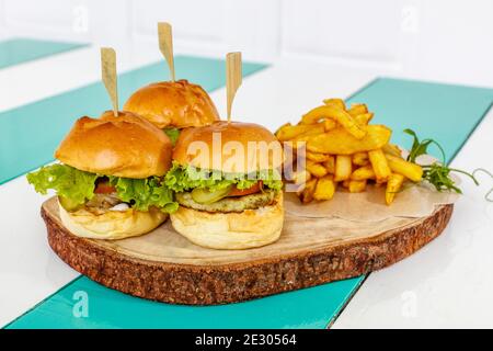 Drei Fischschuppen (Mini-Burger) mit Salat, Tomaten und Gurken, serviert mit pommes frites auf einem Holztablett Stockfoto