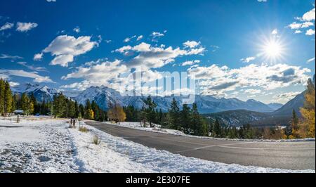 Landstraße im Tal des Waldes in einem verschneiten Herbst sonnigen Tag. Bunte gelbe und grüne Bäume, schneebedeckte Berge. Tunnel Mountain Road, Banff Stockfoto