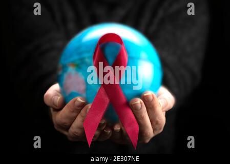 Rotes Band auf Modell des Planeten Erde in Frauenhand auf dunklem Hintergrund für Welt-AIDS-Tag-Konzept. Stockfoto