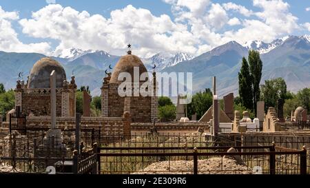 Kochkor, Kirgisistan - 8. Juli 2019: Friedhof mit großen, alten, islamischen Gräbern an einem Sommertag mit Bergen in Kochkor in Kirgisistan. Stockfoto