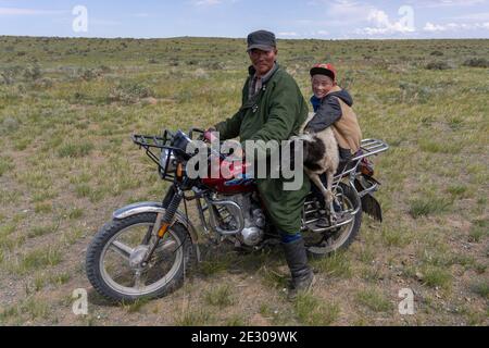 Olgii, Mongolei - 7. August 2019: Mongolischer Mann auf einem Motorrad mit Jungen und Schafen in der Steppe der Mongolei bei Olgii. Stockfoto