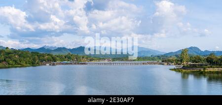 Mon Bridge, längste Holzbrücke im Land über Songalia River und Stausee über Damm in Sangkhlaburi während sonnigen Tages, Kanchanaburi, Thailand Stockfoto