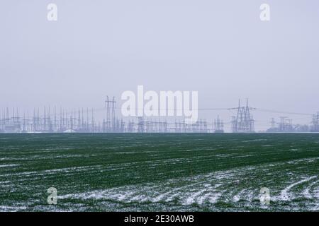 Landwirtschaftliche Landschaft in der Ukraine mit Hochspannungsleitungen und einem mit bewölktem Himmel. Winter Weizenfeld mit Schnee im Winter in Europa. Stockfoto