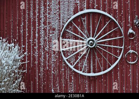 Ein altes Rad hängt an einem alten roten Gebäude aus Holz Wand im Winter Stockfoto