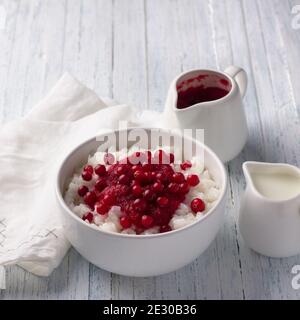 Köstlicher Reispudding mit Preiselbeermarmelade und frischen Preiselbeeren in einer weißen Schüssel auf hellblauem Hintergrund, selektiver Fokus Stockfoto