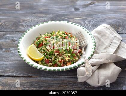 Tabbouleh, traditioneller arabischer Salat aus Bulgur, Petersilie und Tomaten auf einem Holztisch. Köstliche Diät-Essen Stockfoto