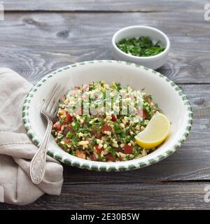 Tabbouleh, traditioneller arabischer Salat aus Bulgur, Petersilie und Tomaten auf einem Holztisch. Köstliche Diät-Essen Stockfoto