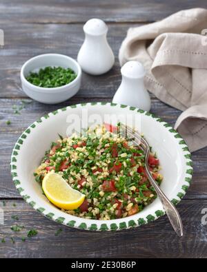 Tabbouleh, traditioneller arabischer Salat aus Bulgur, Petersilie und Tomaten auf einem Holztisch. Köstliche Diät-Essen Stockfoto