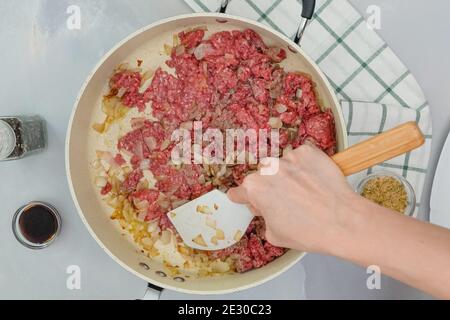 Hackfleisch und gehackte Zwiebel. Koch mischt rohe Zutaten auf der Pfanne. Schritt für Schritt Kochvorgang, Nahaufnahme von oben Stockfoto
