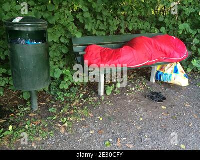 Eine Person, die auf einer Parkbank in einem Wanderschlafsack schläft. Obdachlosigkeit und Flüchtlingskonzept. Stockfoto