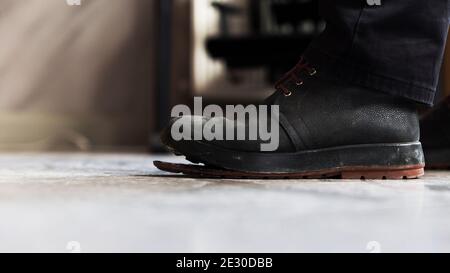 Zentrale Perspektive Low-Angle-Profil Nahaufnahme eines Mannes Fuß mit einem verwitterten Nubuk Boot mit freistehenden Kunststoff-Sohle, stehend auf Estrich Boden. Stockfoto