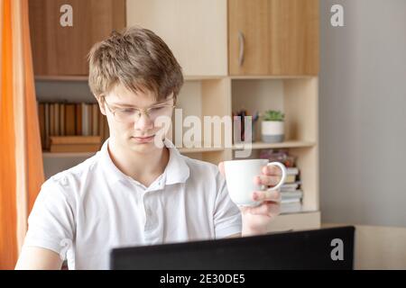 Schüler in Brillen lernen zu Hause mit Laptop. Junger Mann mit Tasse. Home School, Online-Bildung, Home Bildung - Bild Stockfoto