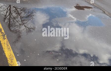 Wolken am Frühlingshimmel spiegeln sich in einer Pfütze. Auftauen. Stockfoto