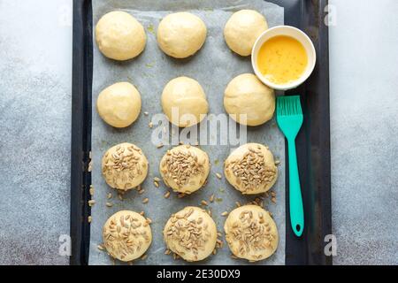 Rohe Teigstücke auf einer Pfanne, Silikonbürste, Ei, Samen. Kochen von hausgemachten Brötchen. Draufsicht - Bild Stockfoto