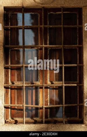 Nahaufnahme eines alten Fensters mit schmiedeeisernen Sicherheitsstangen und hölzernen Fensterläden an einer Steinwand. Toskana, Italien, Europa Stockfoto