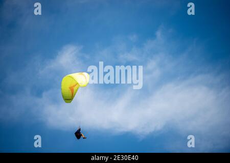 Gelber und orangefarbener Gleitschirm, der in einem blauen Himmel mit Wolken auf dem Hintergrund fliegt. Schwangau, Bayerische Alpen, Deutschland, Europa. Stockfoto