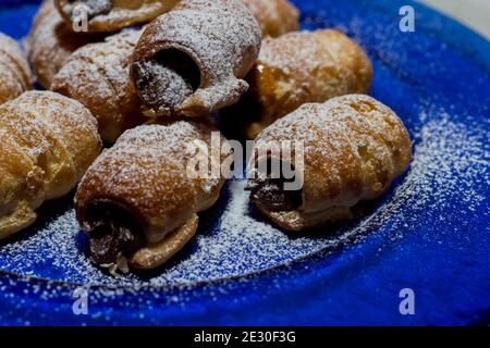 Schokoladenkannoli. Italienische Schokoladenbonbons auf blauem Teller und weißem Hintergrund. Stockfoto