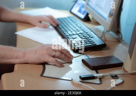 Ein Mann sitzt an einem Computer, hält eine Maus in der Hand, arbeitet zu Hause während der Quarantänezeit, Isolation während einer Pandemie Stockfoto