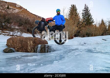 Bärtiger männlicher Reisender Radfahrer im Winter in den Bergen auf einem gefrorenen Fluss inmitten des Eises. Reisen im Winter. Hochplateau Turgen-ASY, Kasachstan Stockfoto