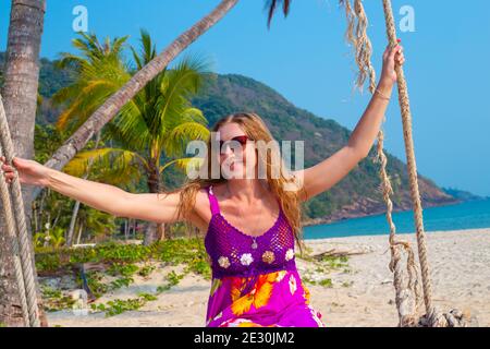 Erwachsene Frau mit langen blonden Haaren schwingend auf einer Schaukel Am Meer auf der Insel Koh Chang in Thailand Stockfoto