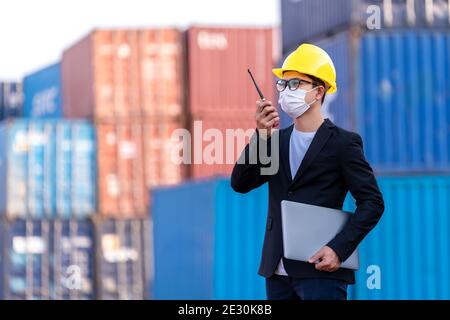 Asiatische männliche tragen eine Maske verwenden Sie ein Radio, um logistische Lager Vorarbeiter Kontrollliste Container-Boxen Befehl. Industrie Import Export Versand Geschäft, Duri Stockfoto