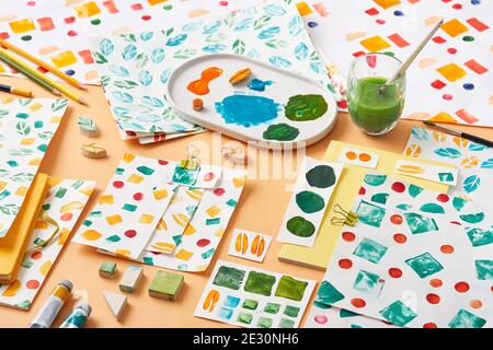 Blatt Papier mit verschiedenen geometrischen Ornamenten und Proben platziert Nahe Palette und Malwerkzeuge auf orangefarbenem Hintergrund Stockfoto