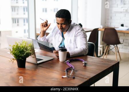 Qualifizierte afroamerikanische männliche Arzt trägt Chirurg Sanitäter Anzug studieren Anamnese Krankheit des Patienten Stockfoto